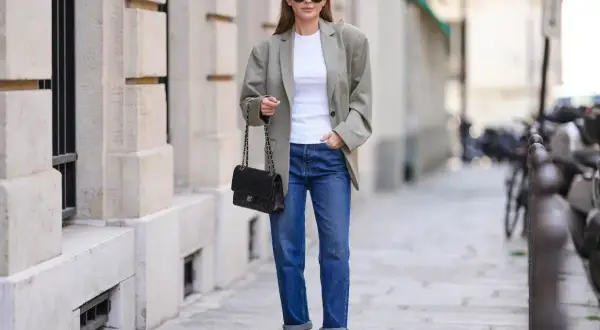 Elegancka kobieta w luźnej marynarce i jeansach, z torebką na łańcuszku. Jej stylizacja to kwintesencja miejskiej elegancji, a brak wzoru w kratę dodaje jej uniwersalności.