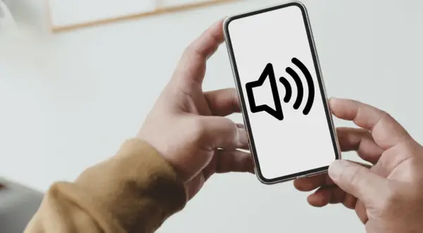 Dłoń trzyma smartfon z ikoną głośnika. Dowiedz się, jak wyłączyć dźwięk klawiszy Samsung, by pisać ciszej.