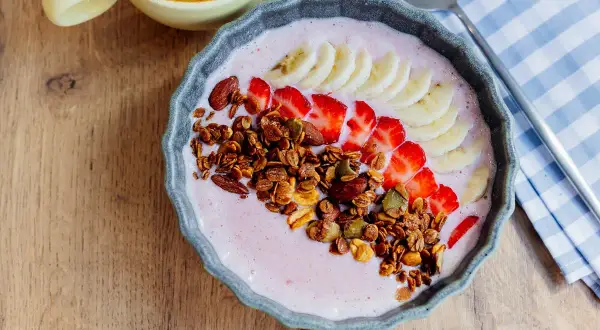 Un delicioso tazón de batido de bayas de acai con fresas, plátano, granola y almendras.