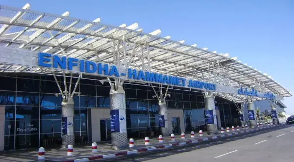 Nowoczesny budynek lotniska Enfidha-Hammamet w Tunezji, z niebieskimi literami nazwy i przeszkloną fasadą.