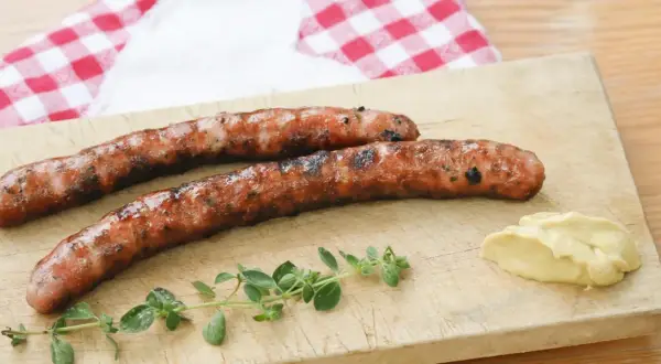 Zwei gegrillte Wildbratwürste auf einem Holzbrett mit Senf und Kräutern. Das beste Wildbratwurst Rezept für einen besonderen Genuss.