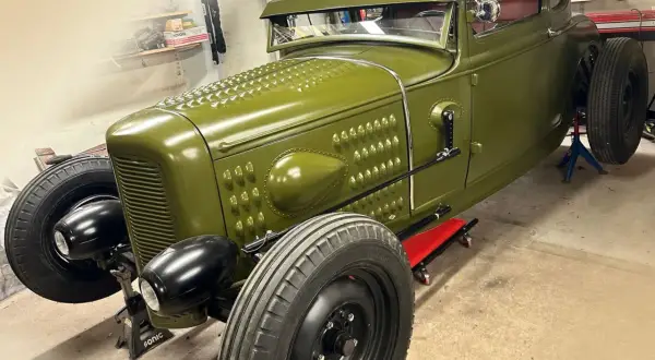 Grön hot rod, en klassisk bilbyggare USA, står på pallbockar i ett garage.