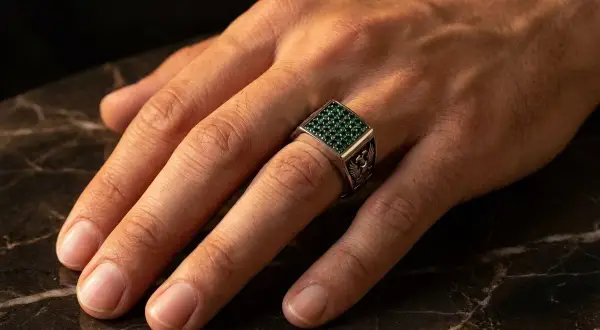 Anillo de plata con piedras verdes, puesto en el dedo anular, el dedo en que se pone un anillo normal.