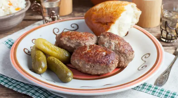 Kotlety mielone z pieczarkami, ogórki kiszone i bułka na talerzu. Pyszny, domowy obiad.