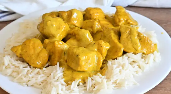 Piatto di riso basmati con saporito pollo al curry, ricoperto da una cremosa salsa gialla.