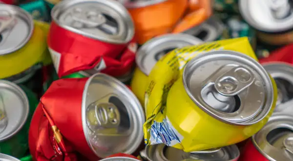 Stos zgniecionych puszek aluminiowych, czerwonych, żółtych i pomarańczowych, gotowych do recyklingu.
