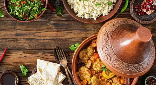 Stół z potrawami w stylu marokańskim: aromatyczny tagine z mięsem, kuskus, sałatka i chleb.