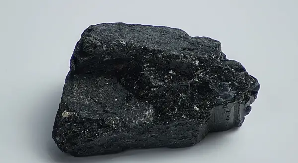 Ein glänzender, schwarzer Stein, der an einen Brocken Onyx erinnert, liegt auf weißem Grund.