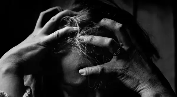 Dłonie zaciskają się na włosach, symbolizując wewnętrzną walkę i dewaluację psychologiczną.