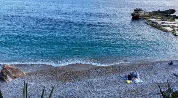 Un mare bello nel nord Italia, con un veliero all'orizzonte e persone che si godono la spiaggia di ciottoli.