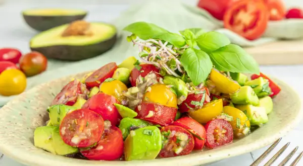 Frischer **avocado tomaten salat** mit Basilikum und Sprossen, garniert mit roten und gelben Kirschtomaten.