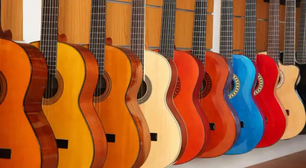 Rząd kolorowych gitar akustycznych, od pomarańczowej po czerwoną i niebieską, prezentuje różne rodzaje gitar akustycznych.