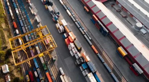 Widok z lotu ptaka na terminal kolejowy, gdzie odbywa się transport intermodalny. Żurawie przeładowują kontenery między pociągami a ciężarówkami.