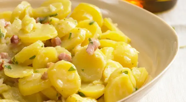 Ein cremiger Kartoffelsalat mit Speck und Petersilie, serviert in einer hellen Schüssel.