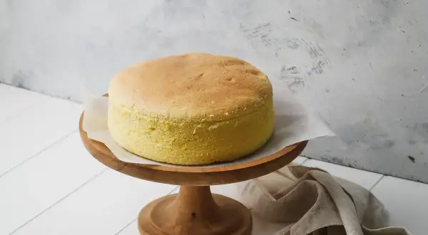Torta soffice e dorata, preparata con albumi montati a neve, su un alzata di legno.