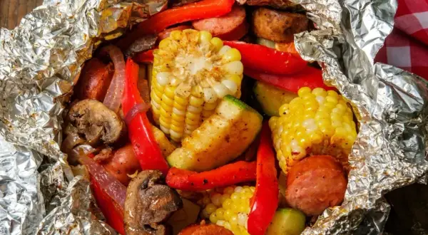 Pyszne sakiewki na grilla z kukurydzą, papryką, pieczarkami i kiełbasą, zapakowane w folię aluminiową.