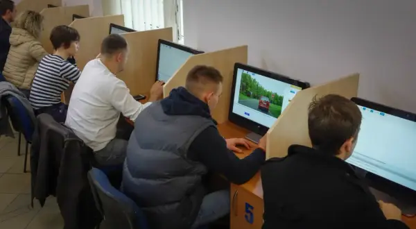 Osoby siedzą przy komputerach, rozwiązując testy. Tak wygląda egzamin teoretyczny na prawo jazdy.