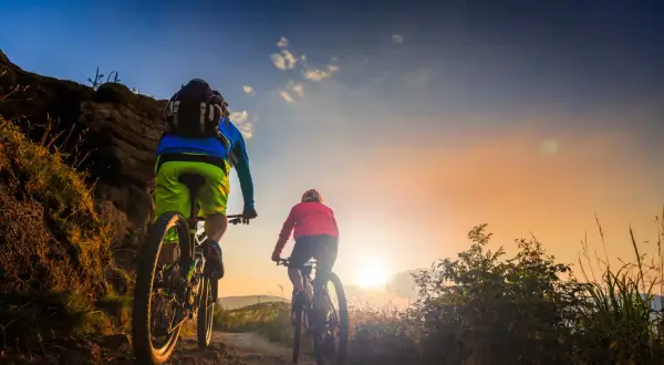 Dwie osoby na rowerach górskich przemierzają malownicze **trasy velo Polska** o zachodzie słońca.