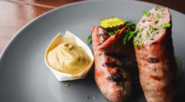 Zwei saftige, gegrillte Bratwürste mit Senf und Gurkenscheiben. Frische Bratwurst wie lange haltbar? Am besten sofort genießen!