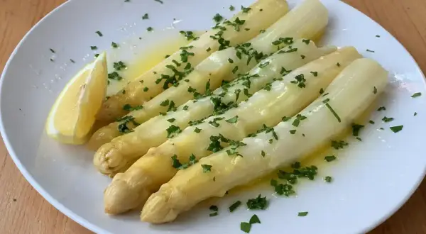 Välkokt vit sparris serverad på en vit tallrik med smält smör, hackad persilja och en citronklyfta. Enkel och god rätt!