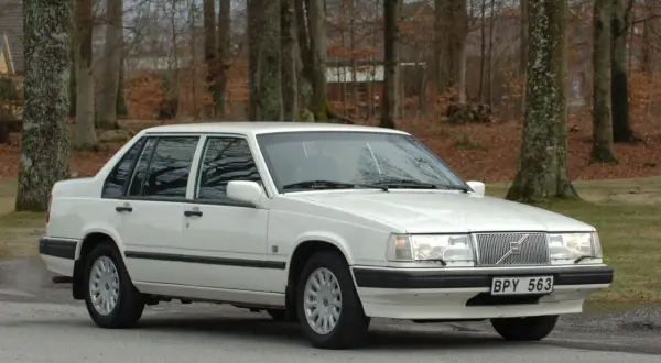 Vit Volvo 940 classic parkerad vid en skogsväg. Bilen är i fint skick med blank lack och kromade detaljer.