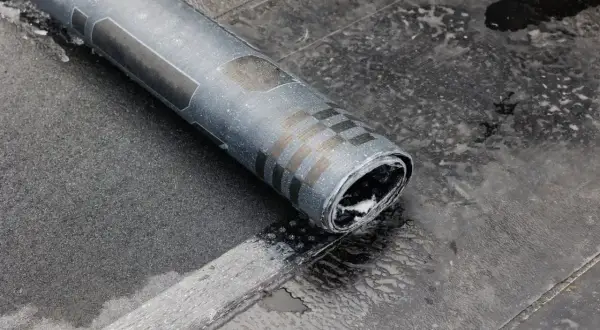 Rolka papy na zimno leży na mokrej powierzchni dachu. Widać fragmenty czarnego materiału i wzory na papie.