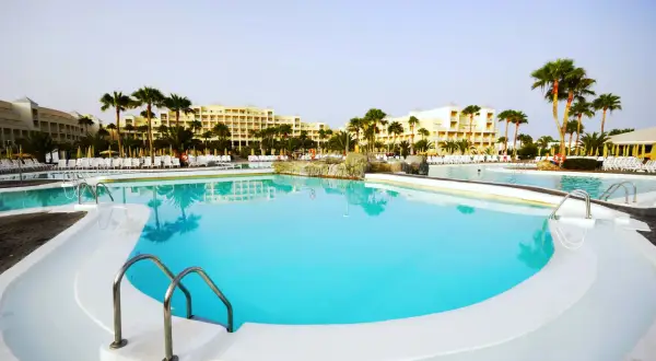 Piscina con acqua cristallina e palme, ideale per una vacanza rilassante. La **clorocaucciù scheda tecnica** descrive i materiali resistenti usati.