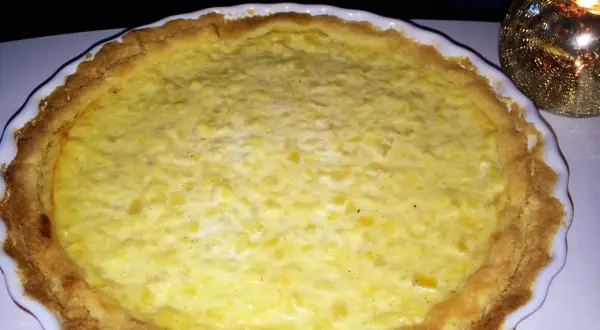 En gyllene ananaspaj glutenfri med en krämig fyllning. En ljuslykta glimmar i bakgrunden.