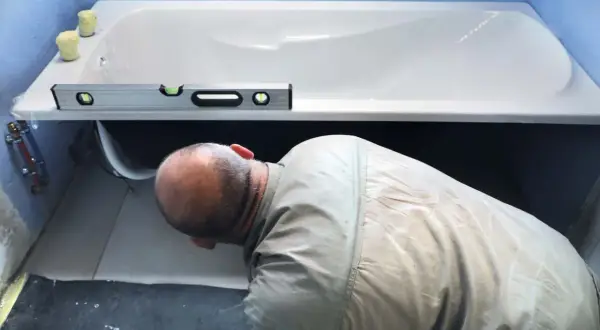Un homme vérifie le niveau d'une baignoire avant de la fixer. L'outil de mesure est posé sur le rebord.