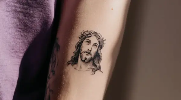 Ein Porträt von Jesus mit Dornenkrone, ein Beispiel für minimalistische Tattoos, auf einem Arm.