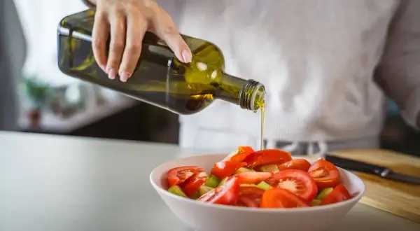 Une main verse de l'huile d'olive cuite sur une salade de tomates. Une touche saine pour contrôler le cholestérol.