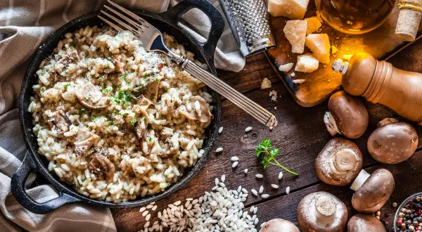 Un cremoso risotto de setas servido en sartén de hierro fundido, con champiñones frescos, arroz, queso parmesano y perejil picado.