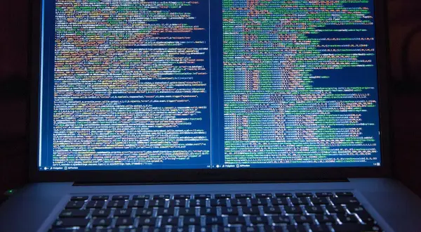 Programista pracuje nad kodem. Na ekranie laptopa widać wiele linii kodu, co pokazuje, co robi programista.
