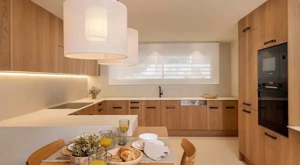 Cocina moderna con gabinetes de madera clara, encimeras blancas y una isla. Perfecta para tus ideas de cocinas.