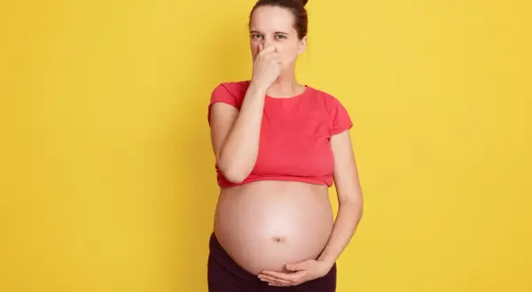 Kobieta w ciąży zatyka nos, cierpiąc z powodu śmierdzących gazów.