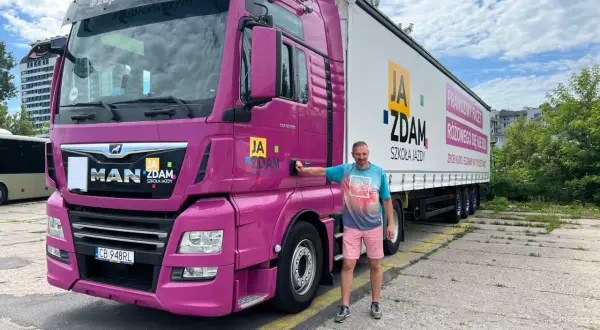 Mężczyzna obok różowej ciężarówki MAN. Na naczepie napis "JA ZDAM SZKOŁA JAZDY". Całkowity koszt prawa jazdy kat C+E do ustalenia w szkole.