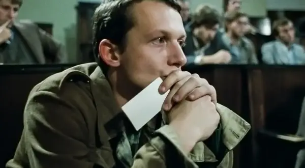 Młody mężczyzna zamyślony, trzymający kartkę przy ustach. Scena z filmu z nurtu **kino moralnego niepokoju**.