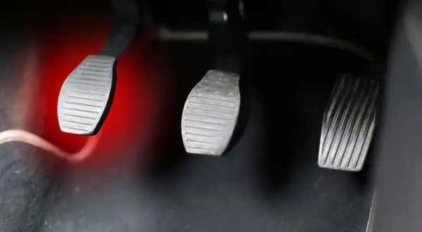 Pédales de voiture, dont celle de l'embrayage, avec une lumière rouge sur la gauche. Le **câble d'embrayage** est visible.