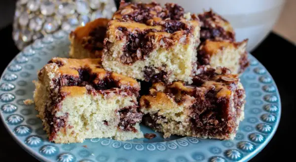 Saftig sockerkaka i långpanna med kanel och nötter, uppskuren i bitar och serverad på en blåmönstrad tallrik.