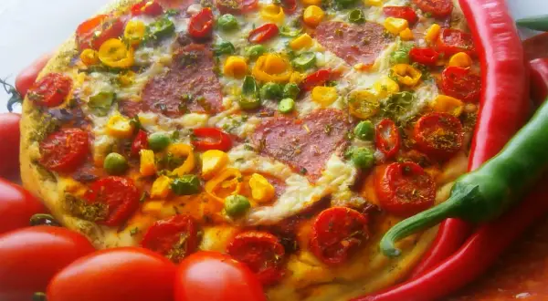 Pyszna pizza pepperoni z pomidorkami, papryką i zielonym groszkiem, otoczona świeżymi papryczkami chili i pomidorami.