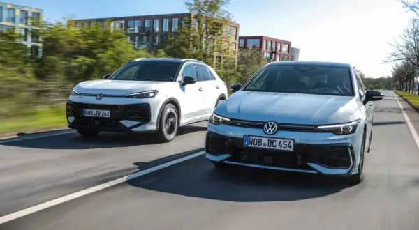 Två Volkswagen-bilar, en vit SUV och en ljusblå sedan, kör på en väg. Den vita bilen ser ut som en t-roc hybrid.
