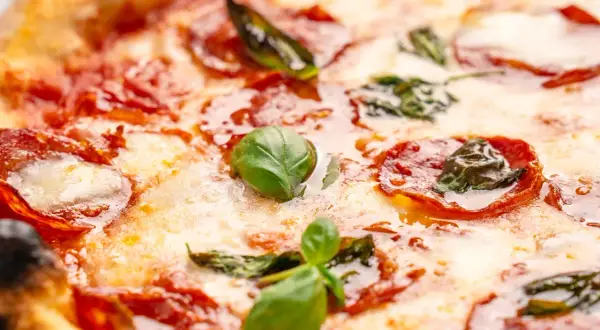 Nahaufnahme einer Pizza mit geschmolzenem Käse, roten Salami-Scheiben und frischem Basilikum. Verschiedene Salami-Sorten machen diese Pizza unwiderstehlich.