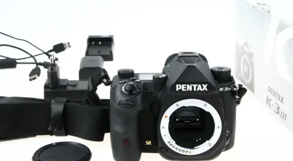 Czarny aparat Pentax K-3 III, ładowarka i akcesoria. Czy to lustrzanka czy bezlusterkowiec? To lustrzanka.