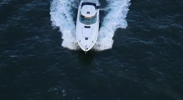 Un bianco yacht naviga veloce, lasciando una scia di spuma. La sua posizione è centrale, in un mare scuro e mosso.