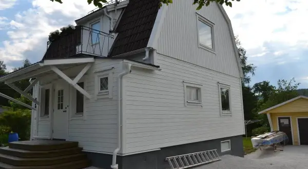 Vitt hus med ny fasad, trappa och en stege redo för arbete.