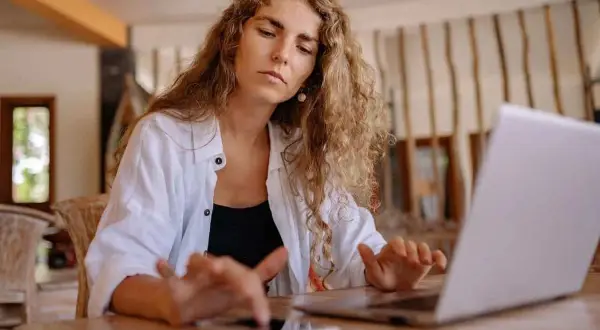 Kobieta z kręconymi włosami pracuje na laptopie i telefonie.