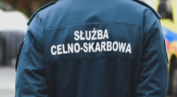 Celnik w granatowej kurtce z napisem "SŁUŻBA CELNO-SKARBOWA" stoi obok pojazdu.