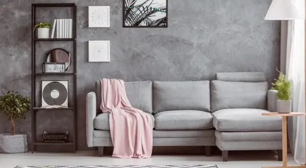 Un divano grigio con coperta rosa, libreria con vinile e piante. Idee su cosa mettere vicino al divano: tavolino, lampada, quadri.