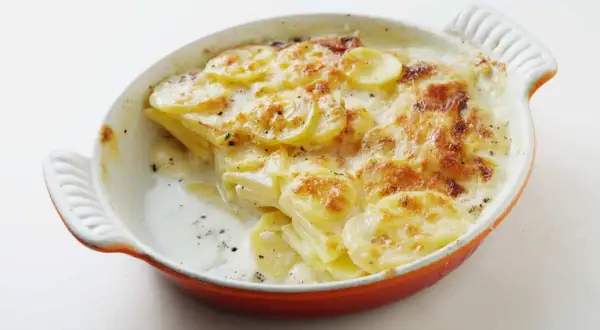 Patatas gratinadas con queso cremoso y dorado, recién salidas del horno en una cazuela naranja.