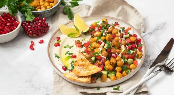 Bunter Kichererbsen Salat mit Granatapfelkernen, Tomaten, Gurken und Hummus, garniert mit Minze und serviert mit Pitabrot.